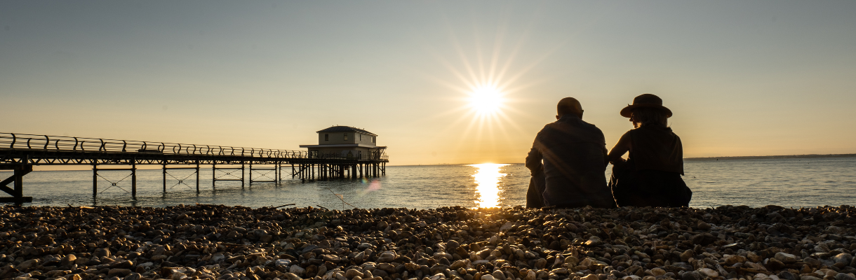 Couple sitting on Totland beach looking at the sunset over the water