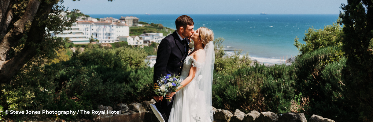 Bride and groom kissing with Ventnor bay in the background at The Royal Hotel on the Isle of Wight
